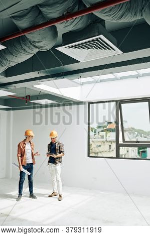 Positive Young Constructin Engineers Standing In Empty Room After Checking Building Acceptance Readi
