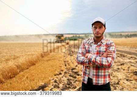 Happy Farmer Proudly Standing In A Field With Arms Crossed On Chest. Combine Harvester Crop Rich Whe