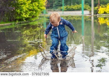 Little Cute Playful Caucasian Blond Toddler Boy Enjoy Have Fun Playing Jumping In Dirty Puddle Weari