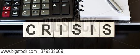 Business Concept Text On Wood Block Crisis With Calculator, Notebook And Laptor On Black Background