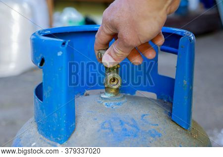 Caucasian Man Opening The Valve On Blue Propan Butan Gas Tank.