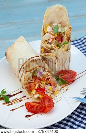 Burrito On A White Plate In A Restaurant. A Quick Meal Of Fried Chicken, Sauce, Red Onions, Corn, To