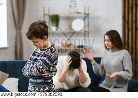 Sad Little Boy Feels Upset While His Parents Fighting At Background. Mother And Father Quarrel. Fami