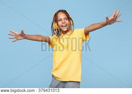 Joyful Little Boy With African Dreads Listening Music In Headphones Dancing Over Blue Background.