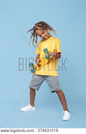 Stilish Little Boy With African Dreads Play On Skateboard Like On Guitar Over Blue Background. Rock 
