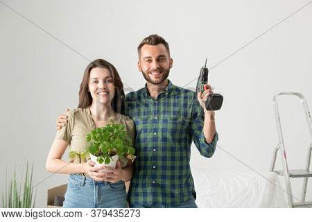 Portrait of cheerful young couple embracing in new apartment and preparing for remodeling after moving
