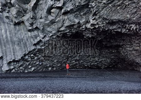 Iceland tourist woman walking on Reynisfjara black sand beach by basalt columns and cave, beach of Vik, South Iceland coast. Happy woman visiting tourist attraction destination.