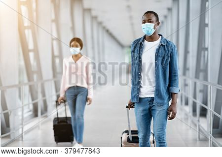 Post-lockdown Travels. Happy African People In Medical Masks Walking With Luggage At Airport Termina