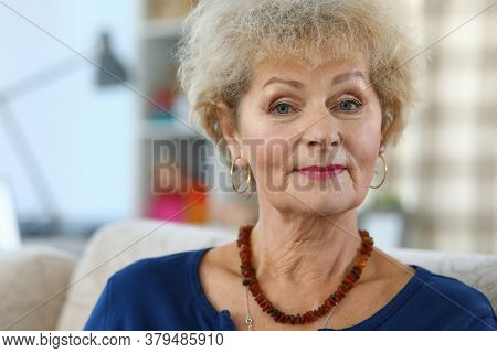Portrait Of A Beautiful Elderly Woman. Grandmother Is Sitting On The Sofa At Home. Kind Look Of An E