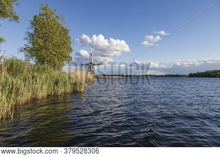 Windmill By The Canal At Glimmen In Holland. The Background Is A Blue Sunny Sky With White Clouds.