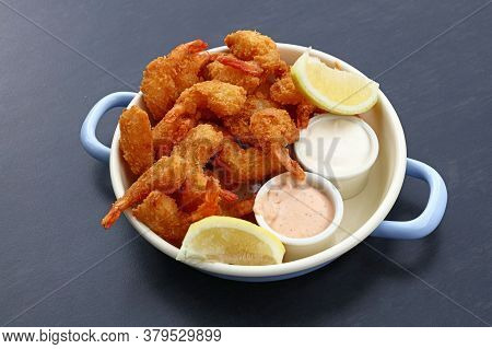 Close Up Portion Of Battered And Breaded Shrimps With Dipping Sauces Served In Cooking Pot Over Blue