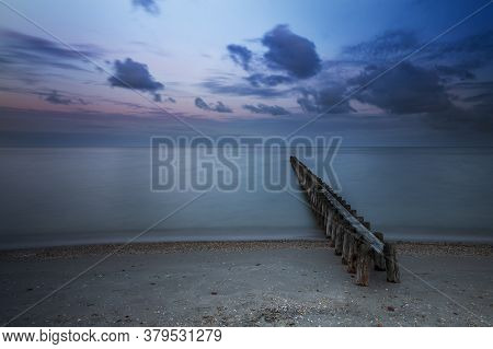 Wooden Breakwater In The Sea At Sunrise In Hindeloopen In Holland. The Sky Is A Blue Sky With Dramat
