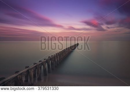 Wooden Breakwater In The Sea At Sunrise In Hindeloopen In Holland. The Sky Is A Blue Sky With Dramat