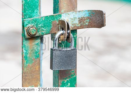 Closed And Locked Door Grill With Silver Padlock. A Metal Lock On Hinges Hangs In Close-up On The Gr