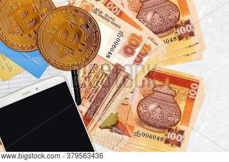 100 Sri Lankan Rupees Bills And Golden Bitcoins With Smartphone And Credit Cards. Cryptocurrency Inv