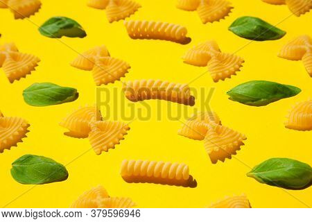 Uncooked Curly Pasta And Basil Leaf Pattern On Yellow Background. Traditional Dry Raw Macaroni Patte