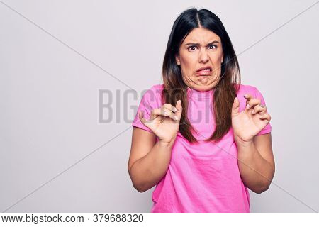 Young beautiful brunette woman wearing casual pink t-shirt standing over white background disgusted expression, displeased and fearful doing disgust face because aversion reaction.