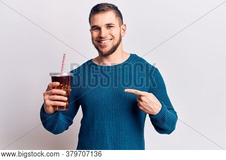 Young handsome man dirnking cola refreshment beverage smiling happy pointing with hand and finger 