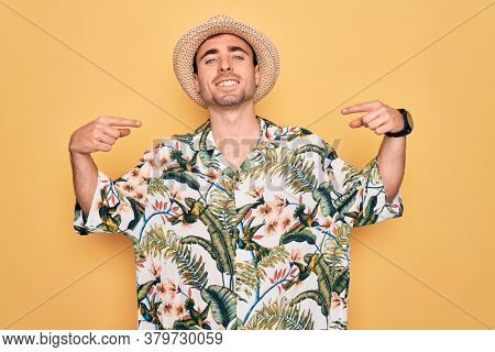 Young handsome man with blue eyes on vacation wearing summer florar shirt and hat looking confident with smile on face, pointing oneself with fingers proud and happy.