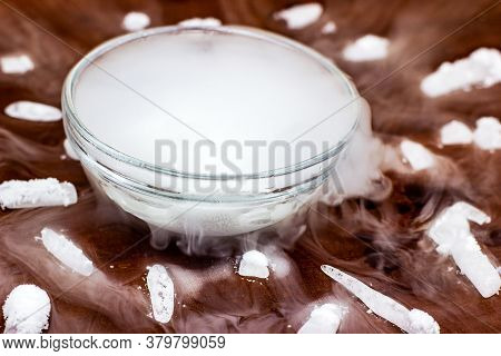 White Cool Dry Ice (frozen Carbon Dioxide) With Smoke Effect In The Glass Bowl On The Dark Brown Woo