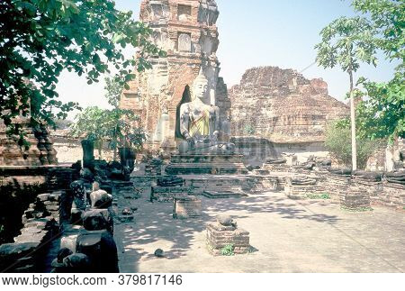 A Sculpture Of The Buddha Sits In Front Of A Buddhist Stupa, Among The Ancient Ruins Of Wat Phra Mah