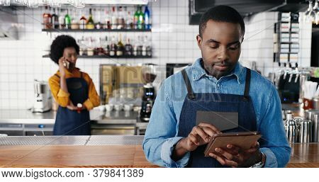 Portrait Of Male African American Barmen Using Tablet Device In Cafe And Smiling To Camera. Handsome
