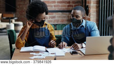 African American Couple In Masks Doing Business Calculations Of Restaurant And Checking Bills. Calcu