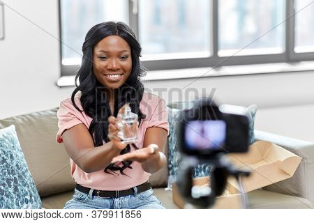 blogging, videoblog and people concept - happy smiling african american female beauty blogger with camera and perfume videoblogging at home