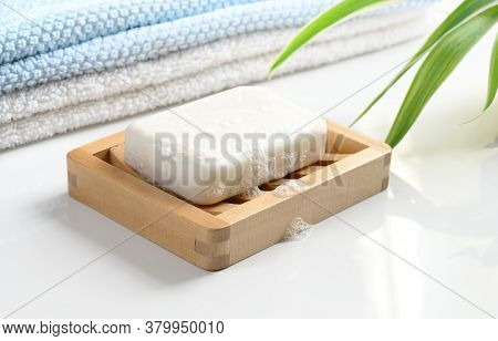 White Soap Bar With Foam On Wooden Soap Dish And Cotton Towels On White Counter Table In The Bathroo