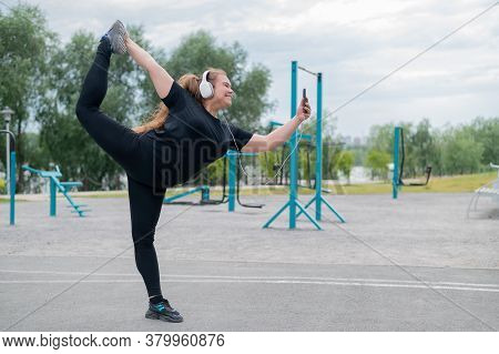 Beautiful Fat Young Woman In Headphones Makes A Figure Skater And Takes A Selfie. A Chubby Smiling G