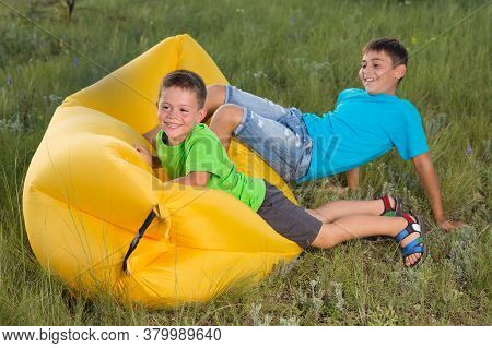 Two Cheerful Boys Outdoors Sitting On Yellow Airy Sofa Having Fun And Laughing, Concept