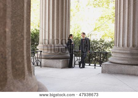 Full length of two attorneys talking outside courthouse