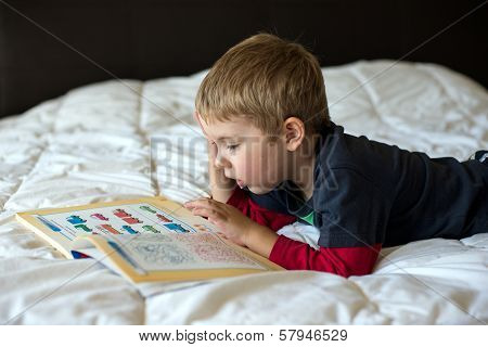 A young blonde boy is learning on a bed