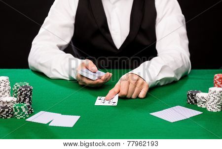 casino, gambling, poker, people and entertainment concept - close up of holdem dealer with playing cards and chips on green table