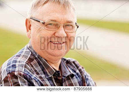 Close up outdoors portrait of smiling middle aged man in glasses and cheered shirt