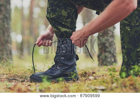 war, hiking, army and people concept - close up of soldier boots and hands tying bootlaces in forest