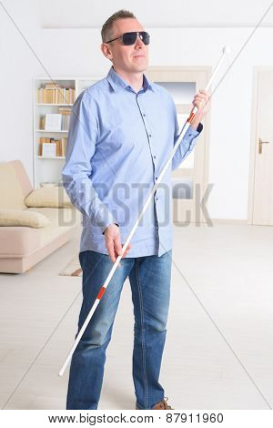 Blind man with white stick and dark glasses at home