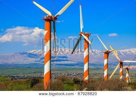 Flowering Golan Heights on a sunny day. Several huge modern windmills. Seen in the distance the snow-covered Hermon. Galilee, Israel
