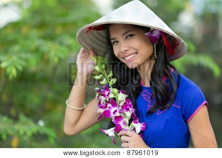 Pretty Vietnamese woman wearing a traditional conical hat holding orchid flower bunch