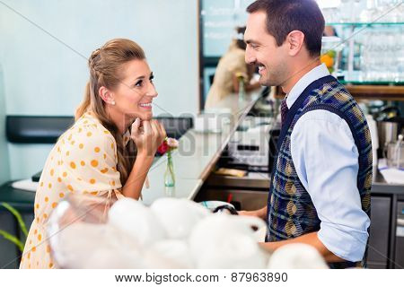 Girl in cafe or coffee bar flirting with barista who is busy preparing Cappuccino with professional machine