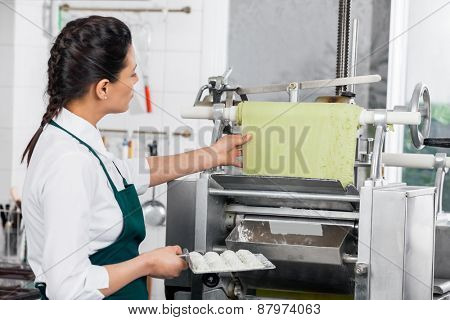 Side view of female chef processing ravioli pasta in machinery at commercial kitchen