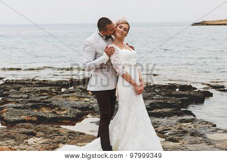 Beautiful  Gorgeous Blonde Bride  And Stylish Groom Kissing, On The Background Of A Sea, Wedding