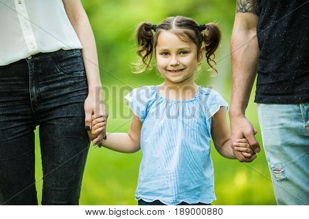 Excited Young Girl Holding Hands While Walking With Parents In Summer Park