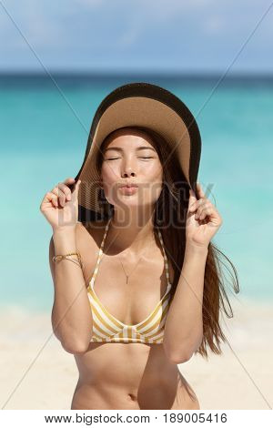 Cute Asian beach woman blowing a kiss holding floppy sun hat on beach vacation summer holidays wearing fashion golden stripes retro bikini outfit. Sepia vintage filter.