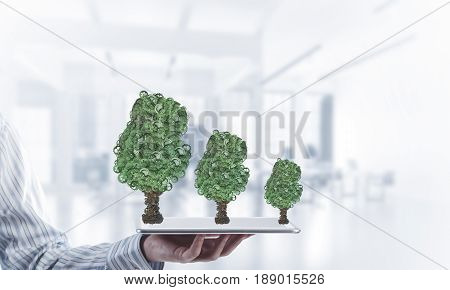 Close of businessman holding tablet pc with green tree made of gears and cogwheels. Mixed media