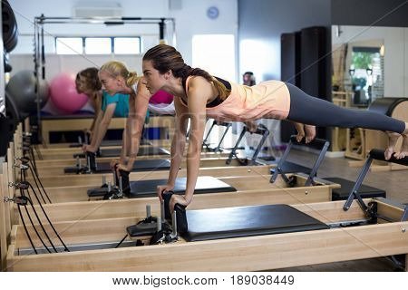 Determined women practicing stretching exercise on reformer in gym