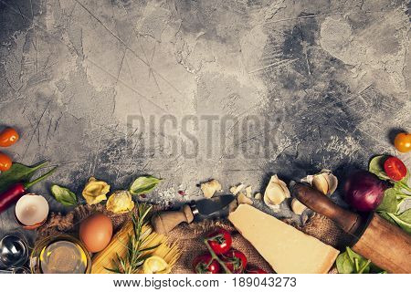 Italian food background with vine tomatoes, basil, spaghetti, spinach, onion, parmesan, olive oil, garlic, peppercorns, rosemary and eggs. Slate background 