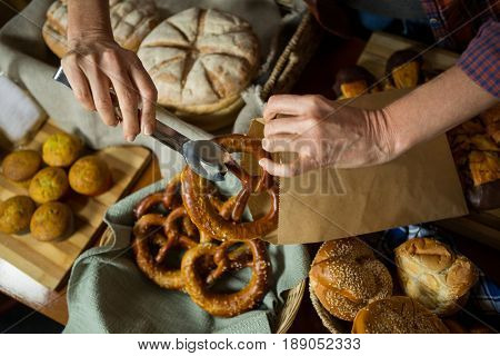Mid section of staff packing pretzel bread in paper bag at counter in bakery shop