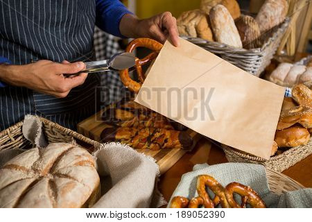Mid section of staff packing pretzel bread in paper bag at counter in bakery shop