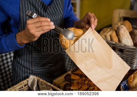Mid section of staff packing croissant in paper bag at counter in bakery shop